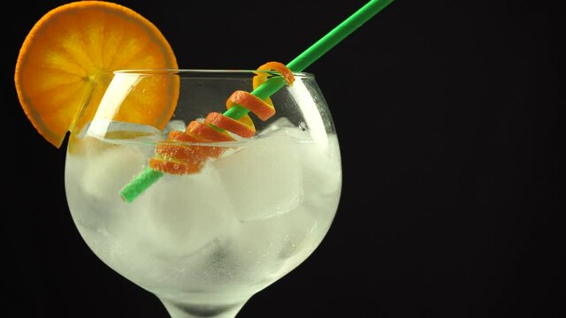 Ice cubes falling in gin orange cocktail with straw, 4k vertical video, close up