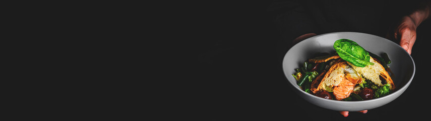 chef in a black suit holds in his hands bowl with salad on Dark grey black background