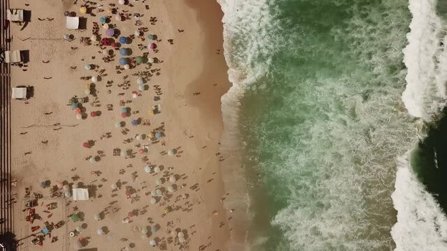 Rio de Janeiro, Brazil, aerial top down view of waves breaking on the shore of famous Ipanema Beach showing colourful beach umbrellas and people enjoying the summer, leblon