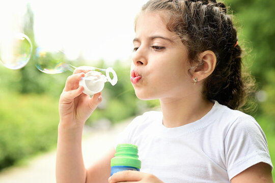 A child plays in the street, a girl blows soap bubbles
