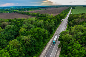 green truck driving on asphalt road through a green forest at sunset. Drone top view. Aerial view landscape.