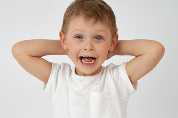 A happy child with blue eyes threw his hands behind his head on a white background. The boy smiles...