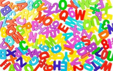 Background from colorful plastic letters and numbers in a chaotic manner on a white backdrop. English alphabet. Children school developmental constructor. View from above. Flat lay. Notebook