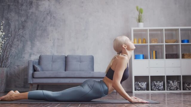 Young and sporty girl in sportswear is doing yoga exercises in home interior. Fit and slender blond woman goes in for sports and fitness. Healthcare, fat burn and wellness.