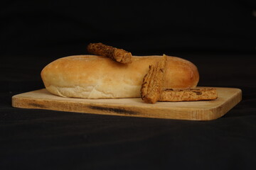 Freshly baked bread and bites on wooden cutting board isolated on black background, rear view