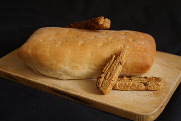 Freshly baked bread and bites on wooden cutting board isolated on black background, rear view