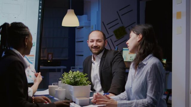 Portrait of businessman looking into camera overworking in company meeting office room late at night. Diverse multi-ethnic workaholics businesspeople analyzing marketing strategy in evening