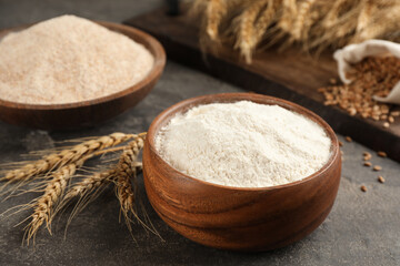 Wooden bowl of flour and wheat ears on grey table