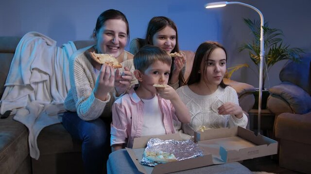 Happy family smiling and laughing while eating pizza and watching TV movie or show at night