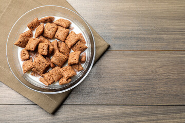 Tasty corn pads with milk in glass bowl on wooden table, top view. Space for text
