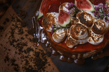 Caramel cake with wild berries, cream and figs on brown background