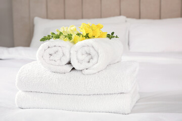 Fototapeta na wymiar Fresh white towels with flower on bed indoors