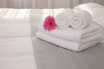 Fototapeta na wymiar Fresh white towels with flower on bed indoors, space for text