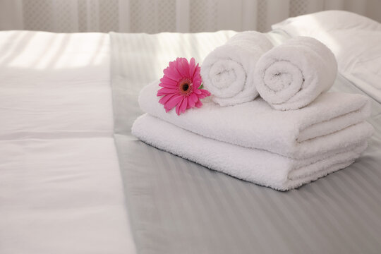 Fresh white towels with flower on bed indoors, space for text