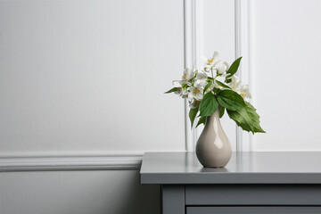 Beautiful bouquet with fresh jasmine flowers in vase on grey table indoors, space for text