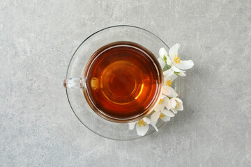 Glass cup of aromatic jasmine tea and fresh flowers on grey table, top view
