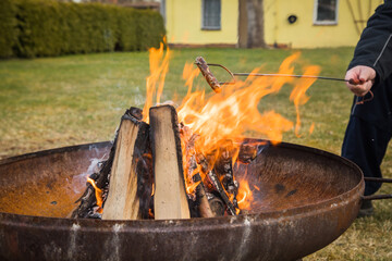 Mann grillt Nürnberger Bratwurst am Spieß über Lagerfeuer Holz Feuer einer Metall Feuerschale im...