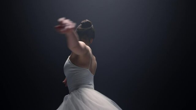 Pretty ballet dancer spinning around indoors. Ballerina dancing in dark space.