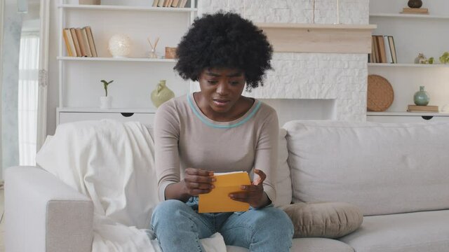 Upset African American ethnic girl feel frustrated open envelope at home reading bad news receive paper post mail letter about financial problem, bank debt bill, failed exam test results or subpoena
