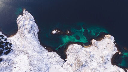 Breathtaking bird's eye view of seashore covered with snow in winter. Aerial top view of scenery rocks, picturesque beautiful nature landscape. Lofoten Island surrounds by Nordic sea