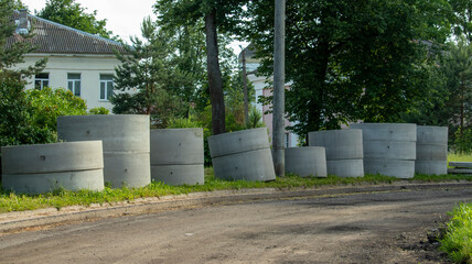 reinforced concrete rings from manholes lie on the grass by the road