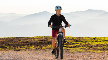 Fototapeta na wymiar Girl child riding mountain bike at sunset. Beautiful golden summer light.