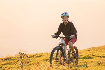 Obraz premium Girl child riding mountain bike into the sunset. Beautiful golden summer light.