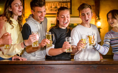 Group of millennials happy friends drinking and toasting beer in Scottish pub - Young teenagers having fun together in a bar restaurant - Concept about teenagers in happy hour celebration time.