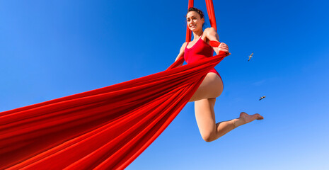 Outdoor activity of cheerful woman training on red aerial silks and ribbons in the sky - Gymnast...