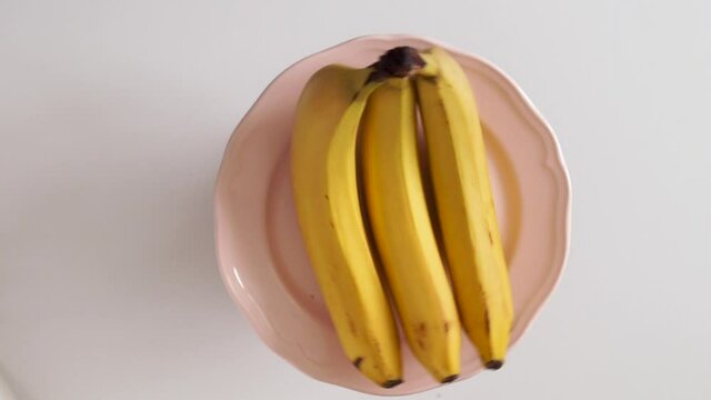 Healthy food diet concept. Three fresh ripe, mellow, mature Bananas rotate on a light pink plate. Rotating fruit plate, top view. HD, vertical, horizontal video. White background. copy space.
