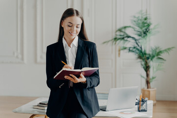 Happy business woman in black formal suit holding note book and smiling