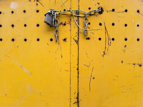 Yellow rusty metal doors clsed by a lock and some electric wires