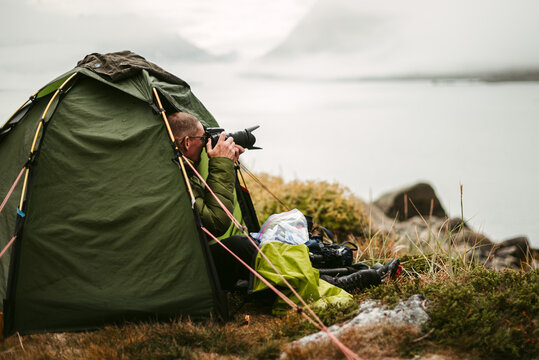 Photographer taking photo of ocean on camera from tent
