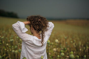 Young pretty girl in back view on the field with poppy seed.