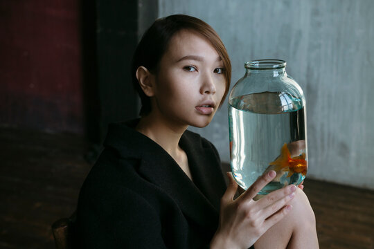 Asian girl with an aquarium fish in a dark room.