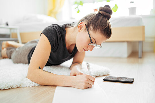 young woman writes in a notebook lying on the floor