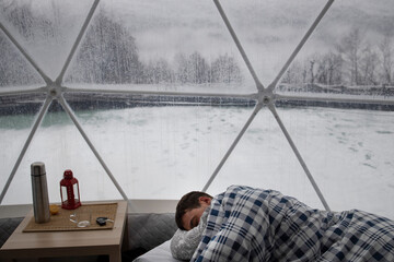 Relaxed man sleeping in spherical camp cupola in winter forest