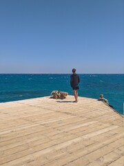 Fototapeta na wymiar Young man standing alone on edge of footbridge and staring at sea