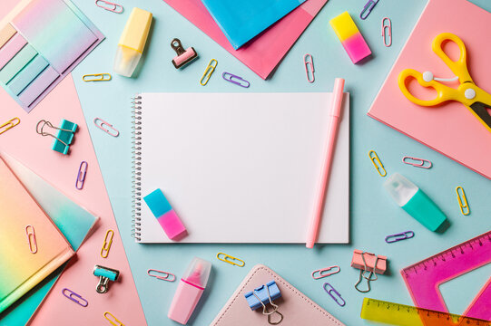 Creative student desk with white sheet of notebook paper and school supplies. Top view with copy space. Back to school flat lay on blue and pink background