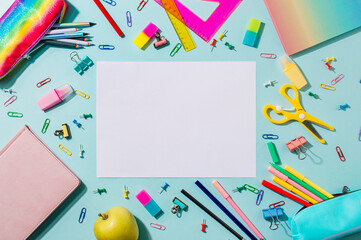 Creative student desk with empty white sheet and colorful modern school supplies on blue background. Top view. Flat lay. Copy space. Back to school concept