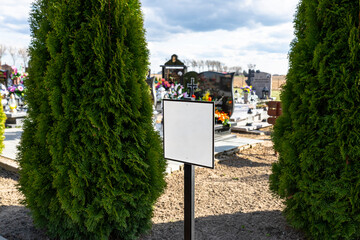 A metal blank plate standing in front of the tombstones in the cemetery between the trees.