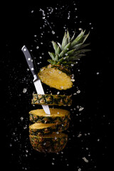fresh and sliced pineapple with a knife with splashes of juice on a black background
