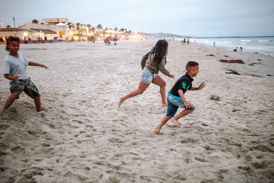 Black mom running with sons toward ocean