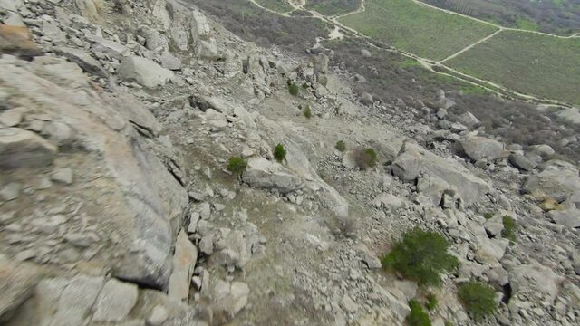 Descent from rocky cliff. Shot. Extreme fast flight from side of rocky mountain on sunny day. Descent by wingsuit or quadrocopter with flight dive on rocky slopes