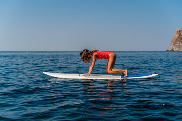 Sporty girl on a surfboard in the sea on a sunny summer day. In a red swimsuit, she sits in the splits on the sap. Summer entertainment on Stortom by the sea