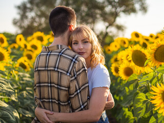 Pareja joven disfrutando de sus vacaciones en un campo de girasoles durante la puesta de sol en...