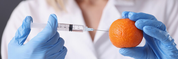 Doctor beautician in gloves making injection into orange closeup