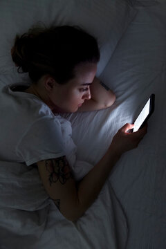 Young woman with smartphone resting on bed at night