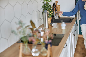 Woman pouring water into glass cup from kitchen sink