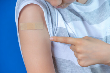 Teenage boy show to adhesive bandage plaster on his arm after vaccination on blue background. Injection covid vaccine, healthcare for children and teenagers